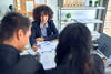 a woman reviews pages of documents with another man and woman at a desk